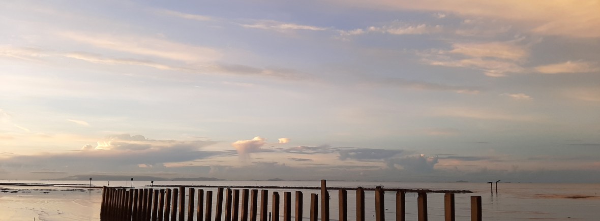 View of beach in Thailand at dawn or dusk with jetty posts sticking out of the water.